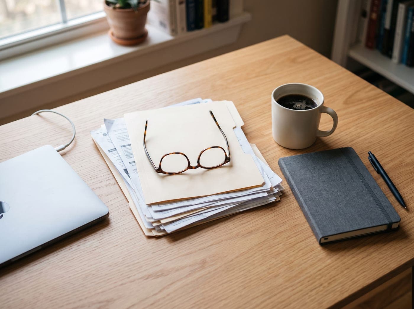 Mesa de trabajo con un montón de facturas, unas gafas de leer y un café